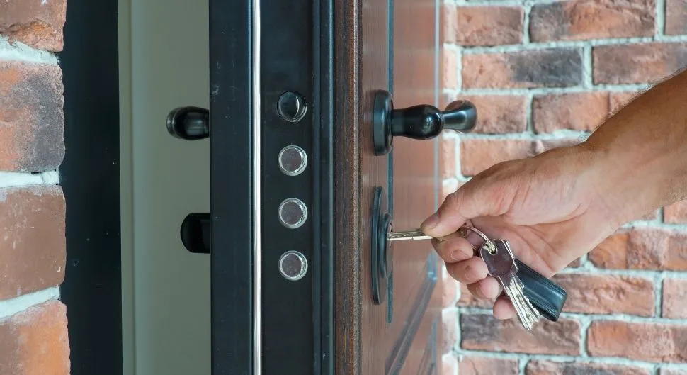 Porte blindée : clé insérée dans le cylindre, pênes de sécurité visibles sur le chant de la porte.